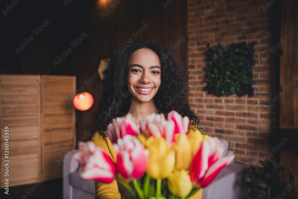 Fototapeta premium Young woman with flowers smiling indoors surrounded by natural light in a cozy home environment