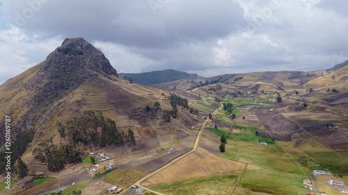 Mountain peak rising above patchwork farmlands and rural dwellings, revealing scenic landscape of Ecuadorian Andean highlands with sweeping panoramic perspective