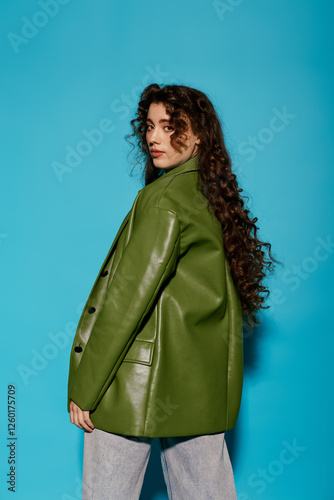 Stylish woman with curly hair poses confidently against vibrant blue backdrop in urban setting