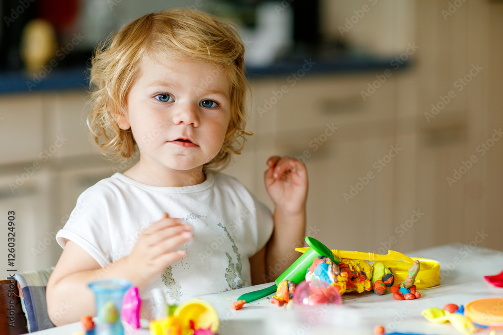 Adorable cute little toddler girl with colorful clay at home. Healthy baby playing and creating toys from play dough at nursery or playschool. Small kid molding modeling clay, creative activity