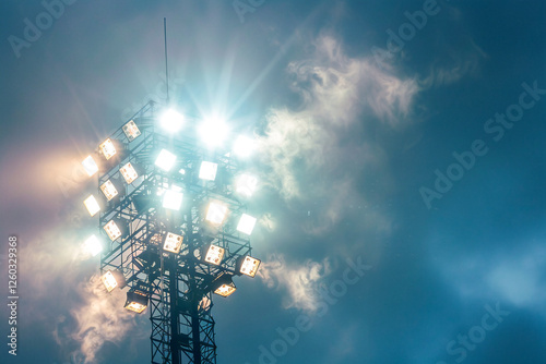 Bright LED stadium floodlights illuminating against a clear blue sky during early evening. photo
