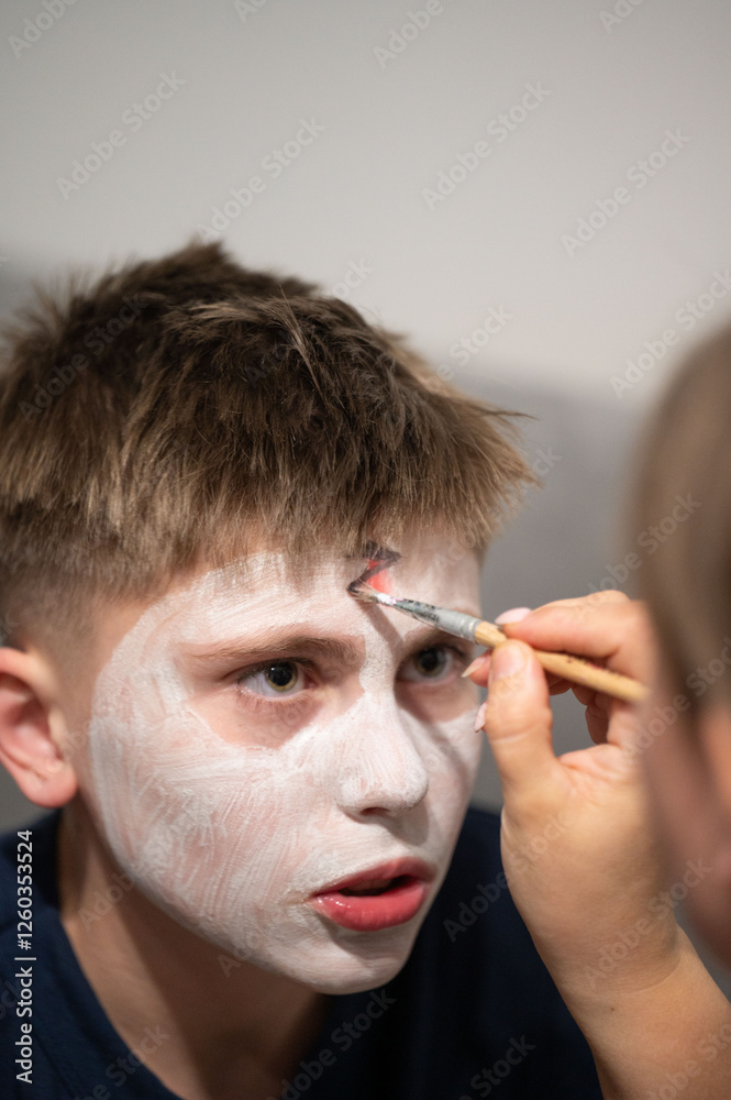 Fototapeta premium Close-up view of a child getting their face painted white by an adult. The setting appears to be a casual indoor environment, perhaps a home.