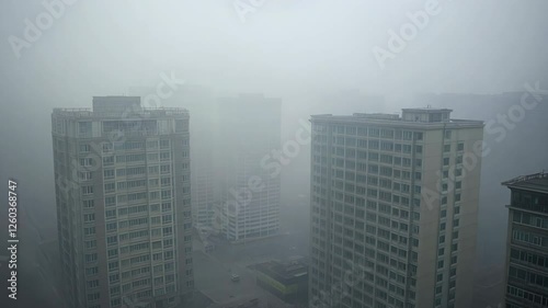 Aerial polluted Chinese city footage, tall buildings covered in thick heavy fog/smog. bird's-eye view. intense air pollution. Man-made smog derived from coal combustion, industrial emissions.