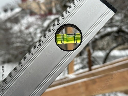 Level tool shows accurate reading of a horizontal surface at a construction site surrounded by snow-covered trees