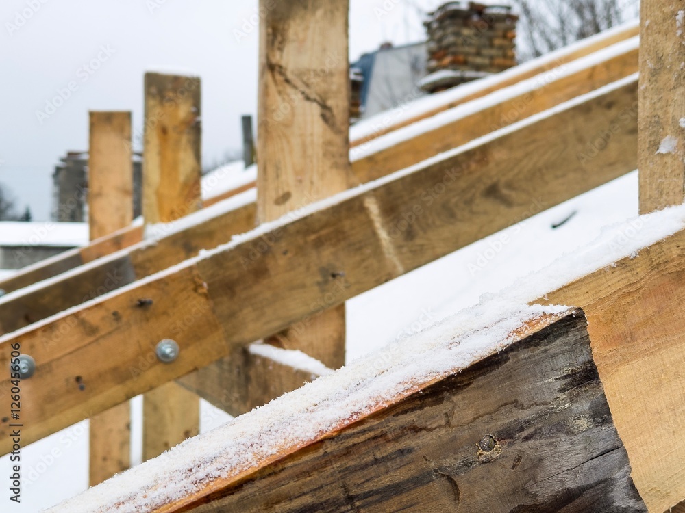Wooden beams are being assembled on a roof in a cold climate where snow is collecting along the wood surfaces Wooden beams are being assembled on a roof in a cold climate where snow is collecting along the wood surfaces