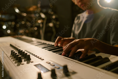 Medium close u p of unrecognizable teenager sitting at keyboard and pressing keys to create melody photo