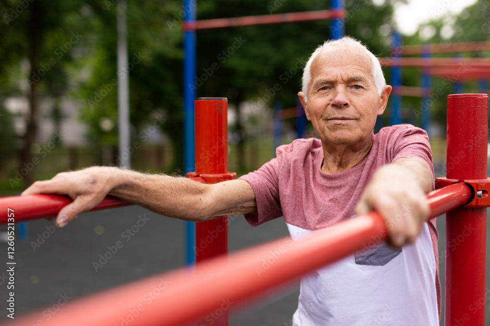 Fototapeta premium Senior sporty man performs various exercises on uneven bars in park