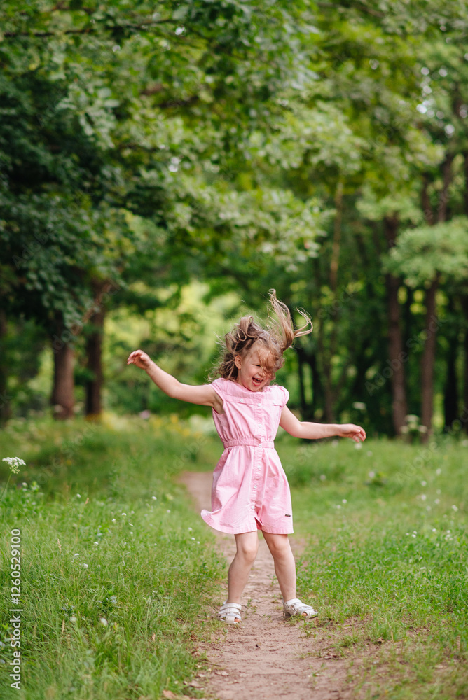 A joyful little girl in a dress jumping with excitement and having fun in a green park on a sunny day A joyful little girl in a dress jumping with excitement and having fun in a green park on a sunny day