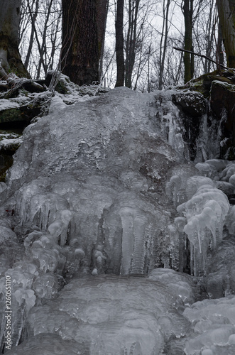 The image features a close-up shot of numerous icicles hanging from a rock cliff. The icicles are various sizes and thicknesses, some are slender and pointy, while others are thicker and more rounded.