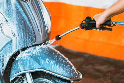 Happy woman washing self-service her motorcycle or motorbike at automatic coin-operated car wash machine. Cleaning of motorcycle or scooter at car wash by water and foam. Selective focus on hands. photo