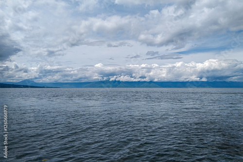 A calm lake with a clear cloudy sky and mountains in the distance