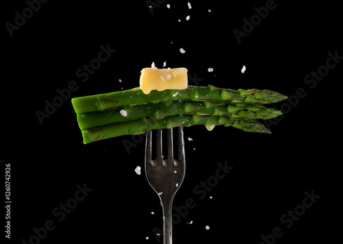 Green asparagus spears, topped with melting butter an sprinkled with salt .on a fork photo