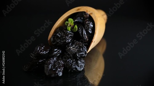 Wooden spoon with prunes and herbs on a black background.