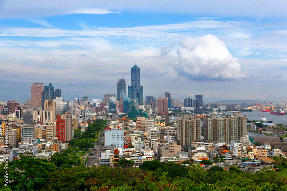 Fototapeta premium Panorama from a viewpoint overlooking vibrant Kaohsiung City in Taiwan, with ships parking in the harbor, a green avenue extending in downtown and landmark 85 Sky Tower standing under sunny cloudy sky