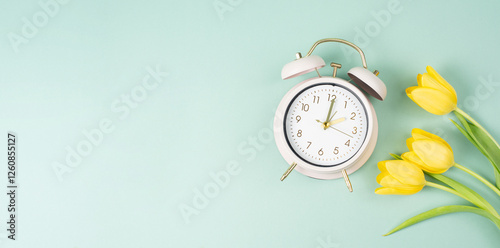 Alarm clock with yellow tulip flowers, switch to daylight saving time in spring, summer time changeover