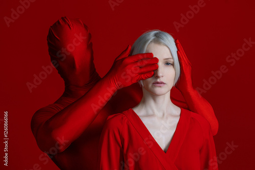 External and internal condemnation. Public opinion turns a blind eye to my needs. A feminist concept. Mysterious red hands surround and cover the eyes and ears of a woman in red, a photo on a red photo