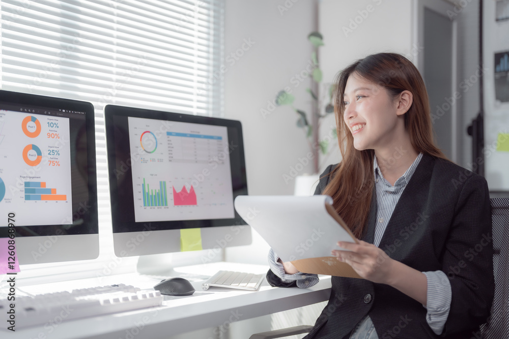 Young professional woman reviewing documents and analyzing data displayed on computer monitors, engaged in business planning and financial analysis in a modern office setting Young professional woman reviewing documents and analyzing data displayed on computer monitors, engaged in business planning and financial analysis in a modern office setting