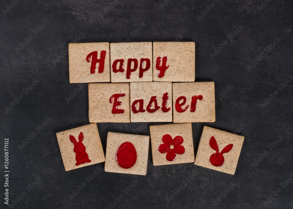 Happy Easter. Square cookies with red marmalade filling in the shape of Happy Easter words, in the shape of Easter egg, flower, rabbit, rabbit ears. Dark background. Top view Happy Easter. Square cookies with red marmalade filling in the shape of Happy Easter words, in the shape of Easter egg, flower, rabbit, rabbit ears. Dark background. Top view