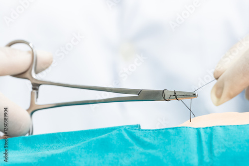 Doctor hand wear sterile gloves and surgery scissor stitching up wound after surgery.Plastic surgeon placing sutures after plastic surgery in operating room.Nurse teaches the technique of suturing.