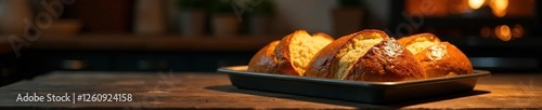 Darkened kitchen with a tray of freshly baked, golden-brown bread on a wooden table, warm, oven