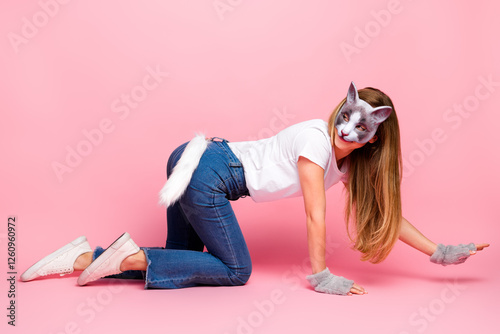 Young female dressed as a cat with a mask and tail posing on all fours against a pink background photo