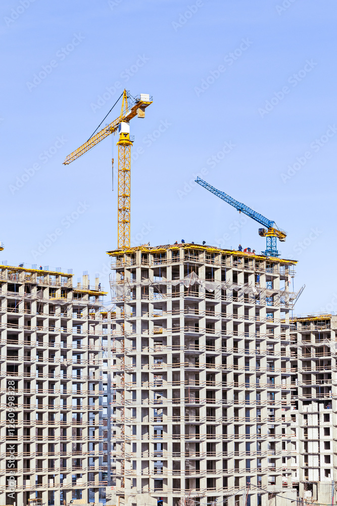 Construction workers on the roof of buildings with cranes in bright daylight Construction workers on the roof of buildings with cranes in bright daylight
