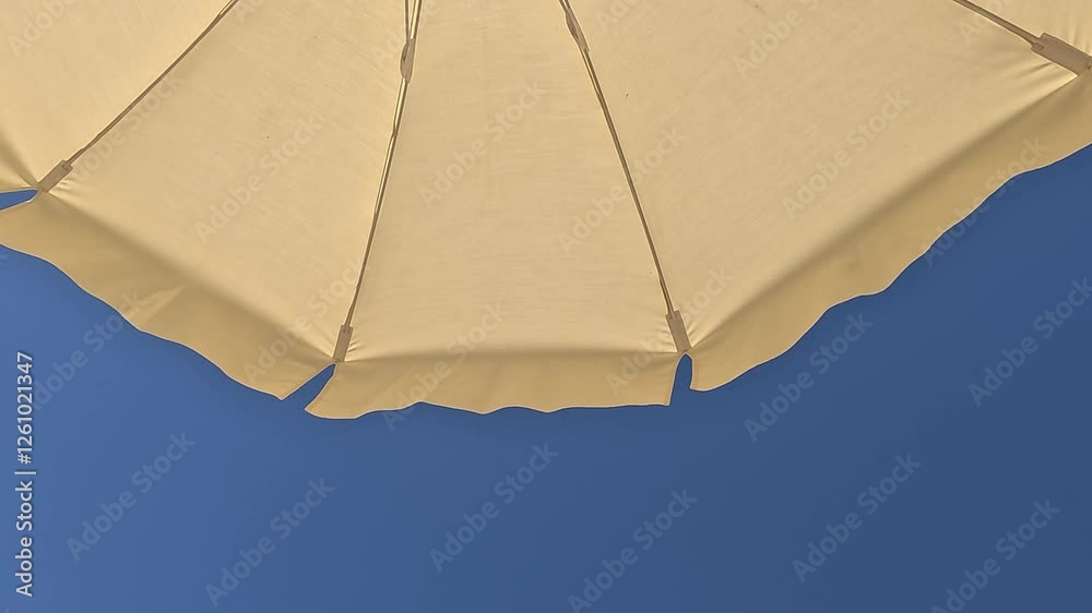 White beach umbrella. Blue sky in the background. View from below. Relaxing context. Summer holidays by the sea. General contest and location