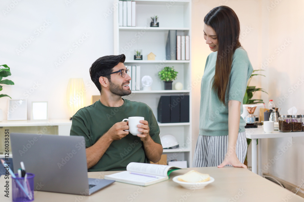 Image of a handsome white man looking at a laptop and working online from home with his girlfriend making him coffee. Image of a handsome white man looking at a laptop and working online from home with his girlfriend making him coffee.