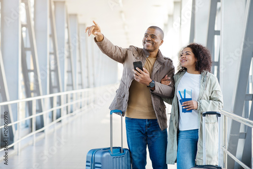 Travel Offer. Happy African American Tourists Couple Pointing Finger Aside Showing Direction Posing With Suitcase Standing At Airport Outside. Vacation Tour Advertisement Concept. High quality photo