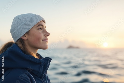 portrait of young sailor gazing out over ocean with sun setting behind them and waves softly blurred