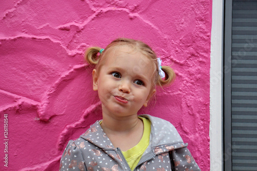Playful Little Girl Making a Funny Face Against a Pink Wall