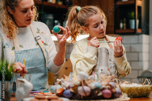 Mother and daughter painting easter eggs together in the kitchen