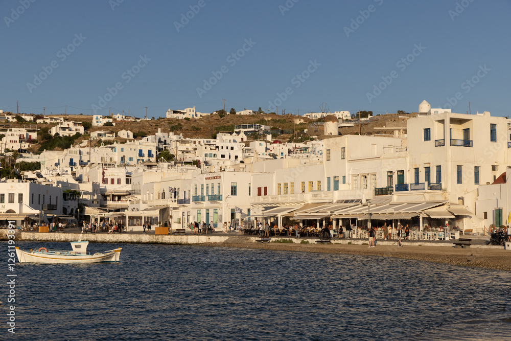 View of white-washed Mykonos seafront from the water during late afternoon. View of white-washed Mykonos seafront from the water during late afternoon.