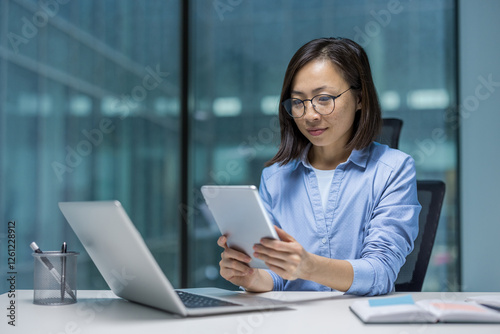 Serious focused woman working with tablet computer, businesswoman sitting at desk inside office at workplace. Employee preparing electronic online presentation report.
