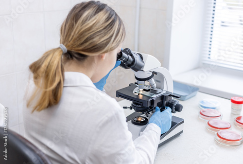 Medical science laboratory: Female biochemist looks under microscope. Scientist studying new virus in laboratory using microscope. Virology during coronavirus outbreak conducting. photo