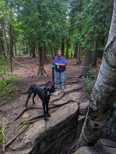 An older woman stand with her black dog in front of a crevice in the forest. On the Bruce Trail along the Niagara Escarpment during summer photo