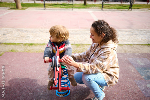Fotografie Smiling Woman Playing with Toddler on Playground Equipment on a Sunny Day