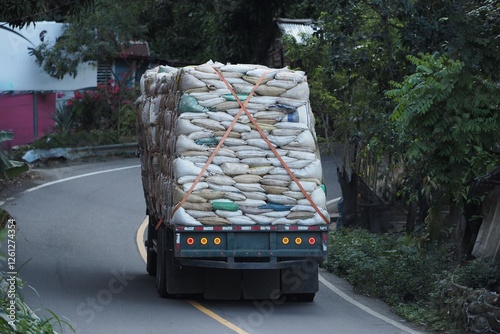 Heavy truck loaded with tightly secured sacks is navigating a curved mountain road.