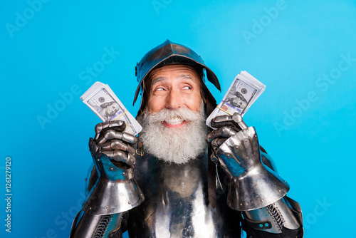 Obraz na plátně Smiling man dressed as a medieval knight raises older age with humor and wealth in piles of cash