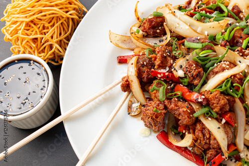 Pieces of chicken thigh marinated and fried in sweet soy sauce with plated peppers and onions, soy sauces and sweet and sour sauce on the side with rashi-type cutlery on top.