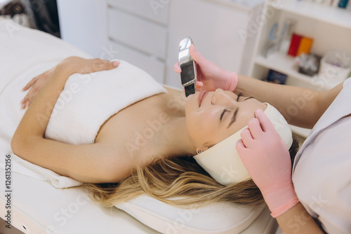 Fotografie Professional cosmetologist using an ultrasound device for facial peeling, provid