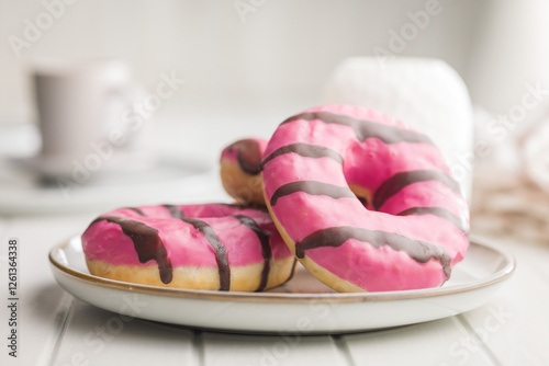 Sweet pink donut with chocolate strips on plate on white table. photo