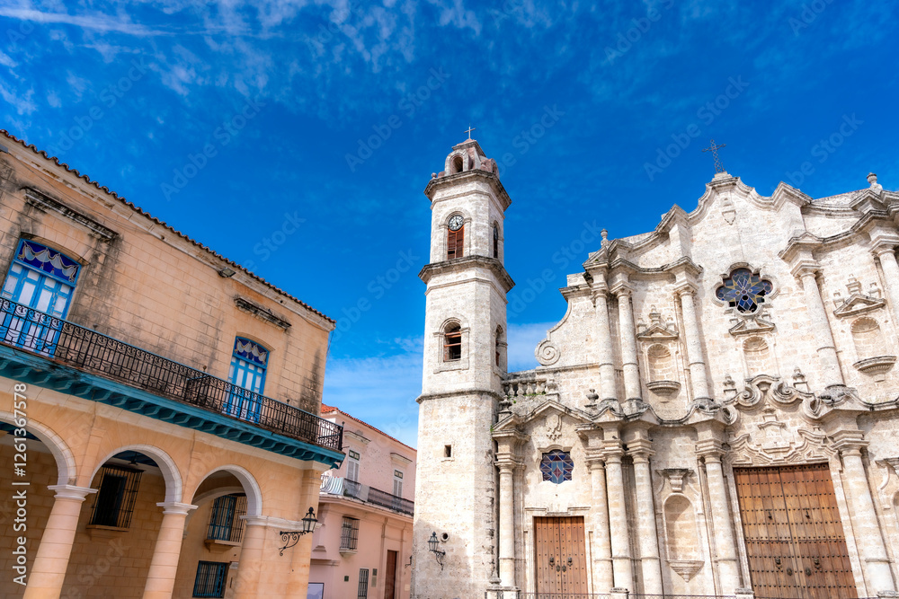 Fototapeta premium The Havana Cathedral, a stunning baroque church in Old Havana, Cuba, stands beside colonial buildings with arched balconies under a bright blue sky. 
