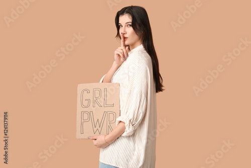 Young woman with sign GRL PWR showing silence gesture on beige background. Feminism concept photo