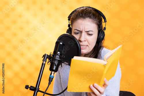 Narrator frowning while reading book, recording audiobook using microphone, playing angry character, studio background. Woman producing digital recording of novel, interpreting furious antagonist photo