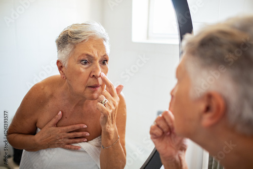 Senior woman looking at mirror in bathroom after shower photo