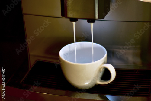 Turquoise cup pouring with two jets of hot coffee from beige espresso coffee machine pump. Close-up of coffeemaker. Coffee latte preparation.