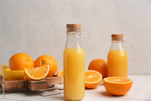 Oranges with juicer and glass bottles of tasty juice on white wooden table