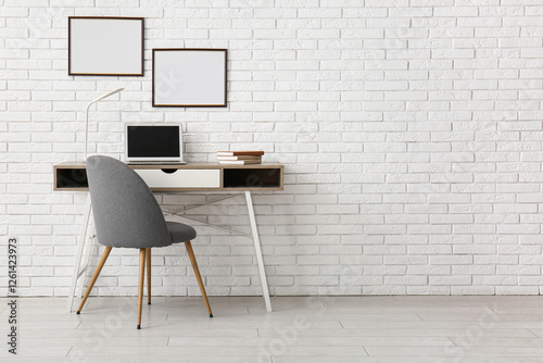 Table with laptop and empty posters on white brick wall