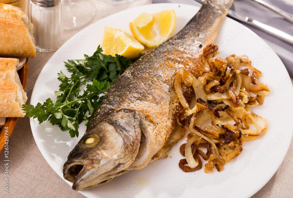 Baked branzino fish with vegetable garnish of grilled onion, slice of lemon and parsley Baked branzino fish with vegetable garnish of grilled onion, slice of lemon and parsley